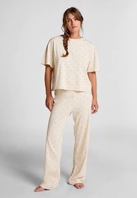 Lichtbeige loungewear-set van zachte stof. T-shirt met korte mouwen en een losse pasvorm, gecombineerd met bijpassende lange broek met een subtiele print.