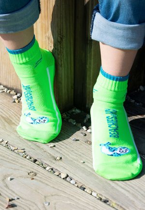 Neon-grüne Knöchelsocken mit blauen Akzenten, die eine Cartoonfigur und den Text "Awesome" zeigen. Hergestellt aus dehnbarem, leichtem Stoff.
