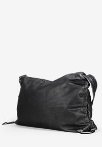 Bolso de cuero negro con una superficie suave y texturizada. Diseño holgado y correa ajustable. Presenta un cierre con cremallera y cordones laterales para dar forma.