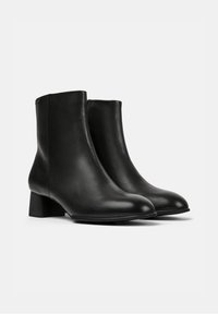 Botas de piel negras hasta el tobillo con una textura suave, punta redondeada y un tacón bloque de altura media. Diseño minimalista sin hardware visible.