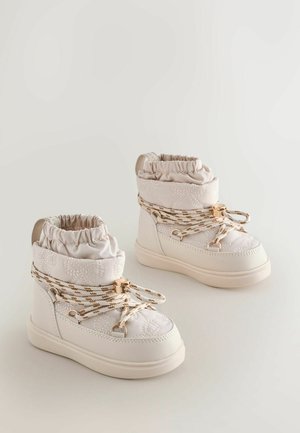 Baltos kulkšninių botų su riešo siuvinėta tekstūra, elastinga apykakle ir auksinėmis raištelėmis. Ypatybės: apvalus pirštas ir guminė pado struktūra, užtikrinanti sukibimą.