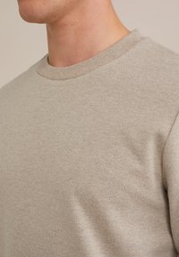 Helebeež värviga ümar kaelusega sviiter, millel on soonikäär ja peen tekstuur, esitades peent mustrit ja pikendatud kuju.