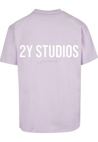 Alyvos spalvos medvilninė marškinėliai su ryškiu baltu užrašu "2Y STUDIOS" ir mažu tekstu po juo. Trumpi rankovės ir apvalus kaklas.