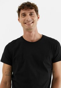 Svart t-shirt med kort ärm i mjuk bomull med rund halsringning. Har en subtil textur och används av en leende person.