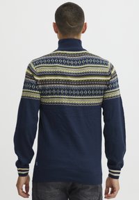 Tengerészeti kék pulóver magas gallérral, színes mintázatú sávval a vállakon és csíkos bordázott mandzsettákkal.