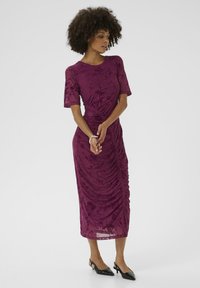 Knee-length dress in deep purple with ruched detailing, featuring short semi-sheer sleeves and a floral pattern. Paired with black slingback heels.