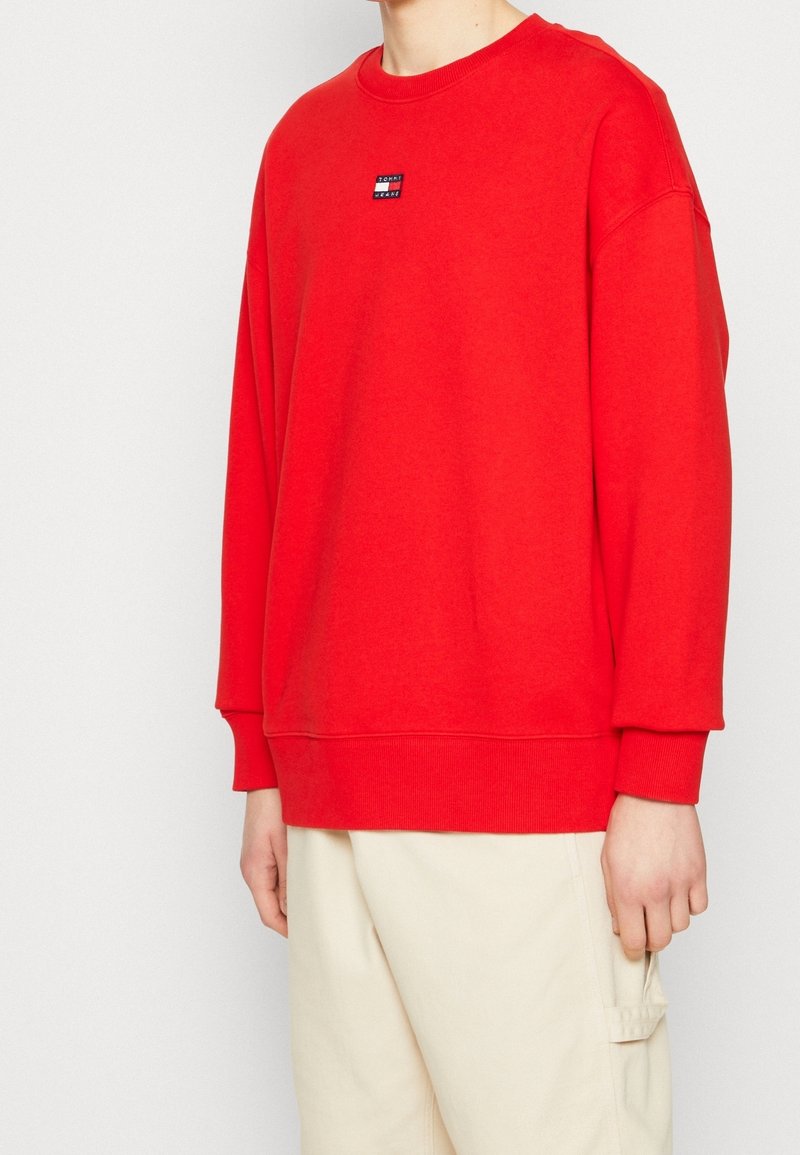 Sweat-shirt rouge avec col rond, coupe oversize et poignets côtelés. Comprend un petit logo cousu sur la poitrine. Tissu doux, design décontracté.