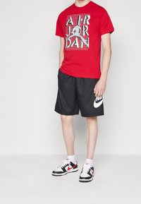 Červené tričko s grafikou "AIR JORDAN", černé šortky s bílým logem Nike, černé a červené tenisky. Neformální sportovní oblečení.