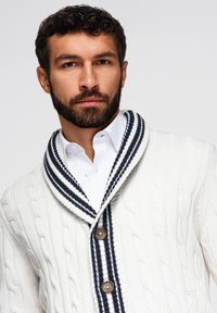 Cardigan bianco a maglia lavorata con colletto a scialle a righe blu navy e bottoni in legno, caratterizzato da una trama testurizzata e una silhouette aderente.