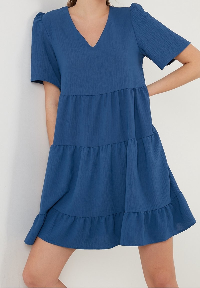 Robe bleu à étages en tissu texturé avec un décolleté en V et de courtes manches bouffantes. Elle présente une jupe évasée et un ourlet volanté.