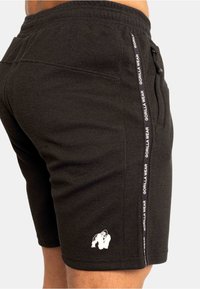 Zwarte sportshorts van textuurstof, met een elastische tailleband, zijzakken en een wit gorillalogo op het linkerbeen. Accentuering met tape aan de zijkant.
