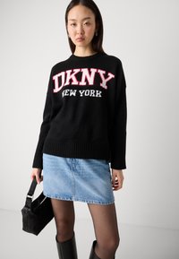 Černý pletený svetr s červeným a bílým nápisem "DKNY NEW YORK", v kombinaci s světle modrou džínsovou sukní a černými kozačkami až po kolena.