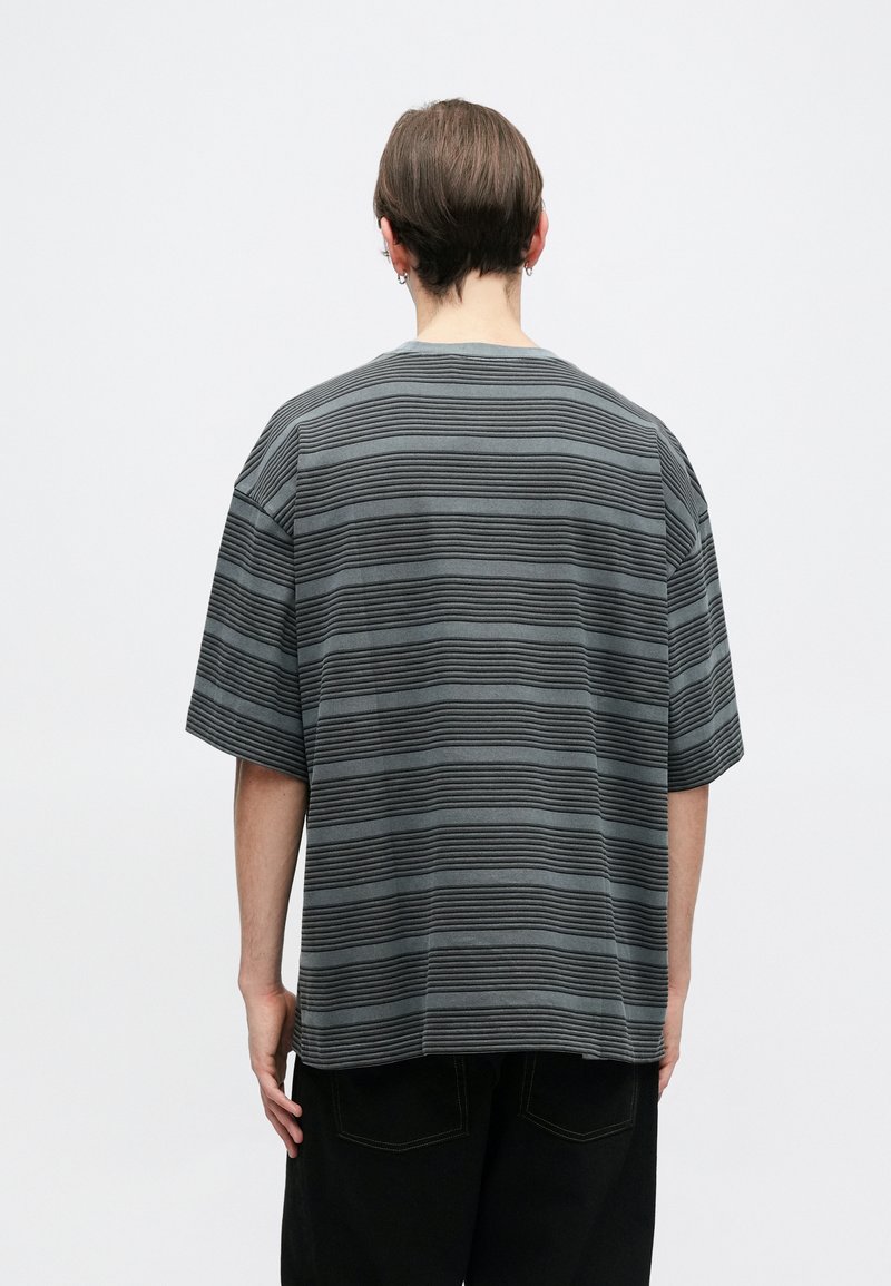 Gray striped short-sleeve t-shirt with a round neck, featuring alternating textured and flat stripes, paired with black loose-fitting pants.