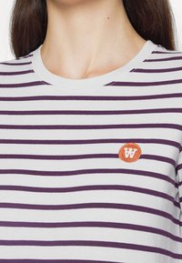 Randig bomull t-shirt med alternerande lila och vita horisontella ränder, rund halsringning och en liten broderad orange logotyp.