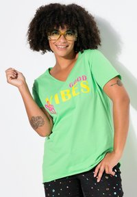 Green cotton t-shirt with "GOOD VIBES" printed in pink and yellow. Short sleeves and a v-neck design. Black pants with colorful sequins.