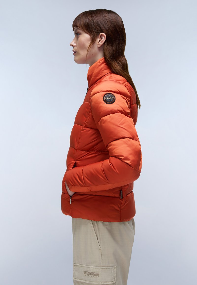 Giacca puffy arancione brillante con colletto alto, design trapuntato, tasche con zip e una toppa rotonda sulla spalla sinistra.