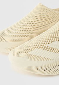Μπεζ παπούτσια τύπου slip-on με 3D εκτυπωμένο σχέδιο πλέγματος που καλύπτει όλη την πάνω επιφάνεια.