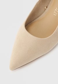 Μπεζ δερμάτινο γοβάκι με μυτερή μύτη, που διαθέτει λεία υφή και χαμηλή κοπή, με μινιμαλιστικό στυλ και χωρίς ορατά μεταλλικά ή διακοσμητικά στοιχεία.