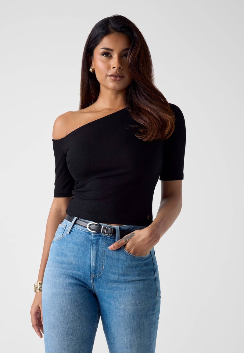 Czarny top na jedno ramię wykonany z prążkowanej tkaniny, zestawiony z jasnoniebieskimi dżinsami. Charakterystyczne detale to dopasowana sylwetka i czarny pasek.