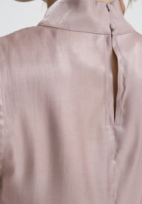 Ingrandimento del retro di una blusa di satin rosa pallido con colletto alto e piccoli bottoni rivestiti in tessuto che chiudono un'apertura a forma di chiave.