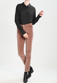 Černobílá kostkovaná košile s dlouhým rukávem omotaná s růžovými manšestrovými kalhotami a čern ými kotníkovými botami na podpatku.