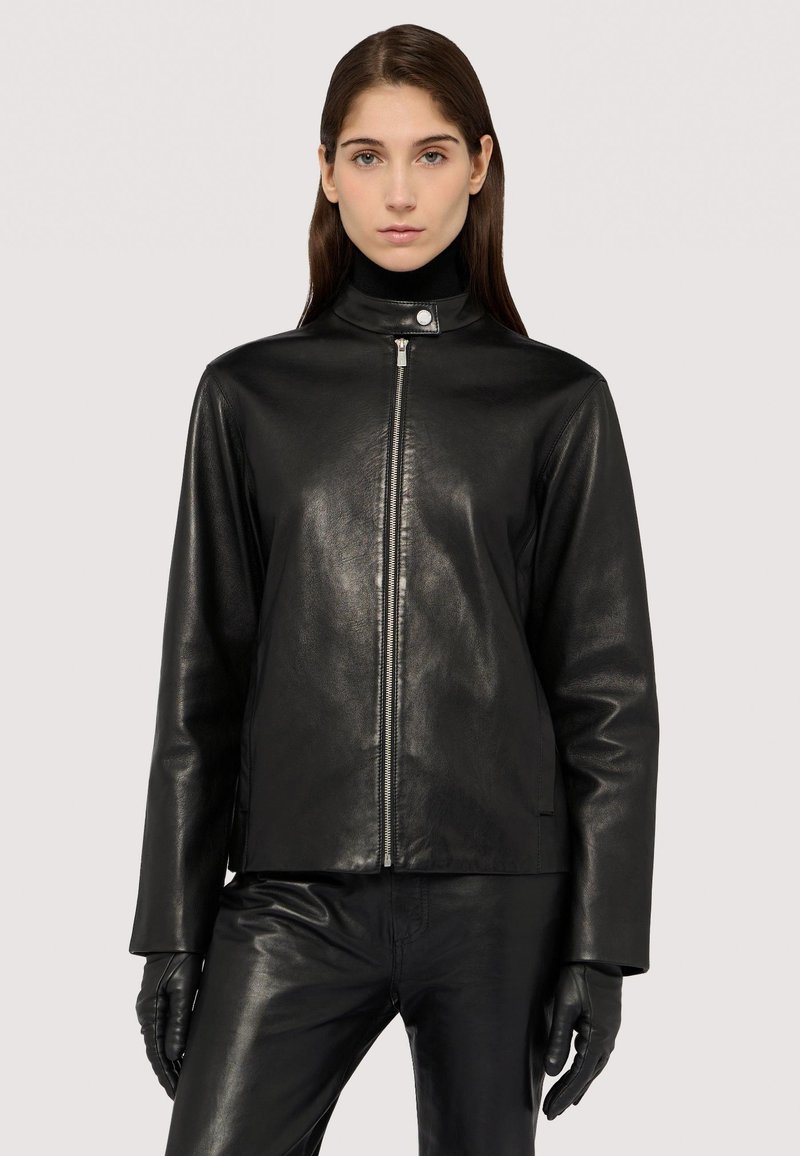 Schwarze Lederjacke mit hohem Kragen, Reißverschluss vorne und langen Ärmeln. Glatte Textur und minimales Zubehör, kombiniert mit schwarzen Lederhandschuhen.