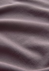 Měkká fialová textilie, která se vyznačuje hladkým povrchem s jemným leskem a jemným tkaním, vytvářejícími jemné vlny a záhyby.