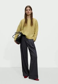 Light yellow oversized sweater, gray wide-leg trousers, and red pointed shoes. The model holds a textured black bag.