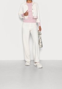 Giacca di denim bianca, maglietta a maniche lunghe a righe rosa chiaro, pantaloni bianchi a gamba larga e sneakers bianche chunky. Tiene una borsa con stampa pitone.