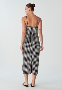 Čierno-krémové kockované midi šaty s tenkými ramienkami, priliehavým strihom a rozparkom vzadu, vyrobené z hladkej tkaniny.