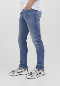 Jeans azzurri chiari con una vestibilità slim, realizzati in denim, caratterizzati da una leggera scoloritura e cuciture a contrasto. Abbinati a scarpe da ginnastica bianche e nere.