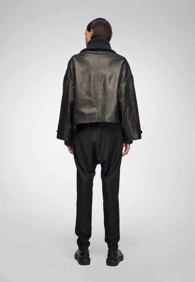 Black leather cropped jacket with wide sleeves, featuring a high ribbed collar. Paired with black loose-fit pants and black shoes.