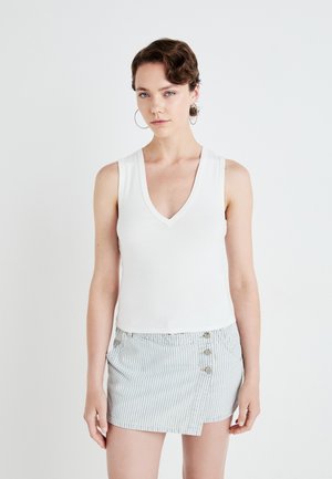 Witte, geribbelde mouwloze top met een V-hals, gecombineerd met een lichtblauwe, gestreepte minirok met een knoopdetail aan de zijkant.