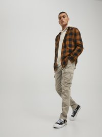 Flannel shirt in orange and black check pattern, beige cargo pants, and black sneakers. Hoodie under the shirt, standing posture.