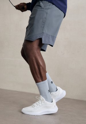 Baskets de sport blanches avec une tige en mesh texturé, associées à des chaussettes bleues claires à côtes avec un logo. Shorts de sport gris avec des bordures perforées.