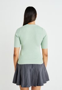 Haut ajusté à manches courtes en jersey côtelé de couleur vert clair, associé à une jupe grise évasée. Texture lisse avec un col rond.
