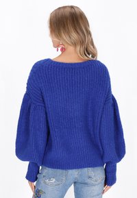 Maglione azzurro oversize a maglia con texture a coste, maniche ampie e scollo a barca, abbinato a jeans azzurri chiari con ricami floreali.