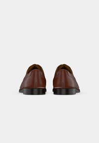 Chaussures en cuir marron avec une texture lisse, bout arrondi et petit talon noir, vues de l'arrière, mettant en valeur les détails de couture et un design minimaliste.