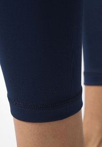 Marineblaue Leggings aus dehnbarem Stoff mit einer enganliegenden Passform, die eine glatte Textur und subtile Nahtdetails am Saum aufweisen.