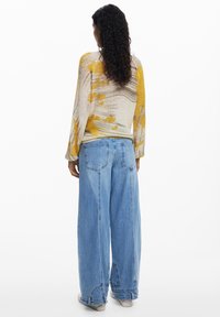 Gebreide trui met een abstract patroon in geel, grijs en wit; gecombineerd met lichtblauwe, hoge taille, losse jeans; getextureerde brei-details.
