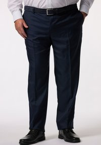 Pantalones de vestir azul marino con una textura suave, que presentan pliegues frontales, bolsillos laterales y una cinturilla plana. Combinados con zapatos negros.