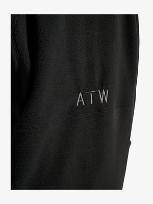 Schwarzer Fleece-Stoff mit weißen bestickten Großbuchstaben „ATW“ auf der Rückseite, zeigt strukturiertes Material und Nähdetails.