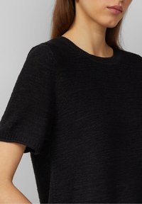 Pull noir à manches courtes avec un col côtelé, fabriqué à partir d'un tissu texturé, présentant une coupe décontractée et de fines lignes horizontales.