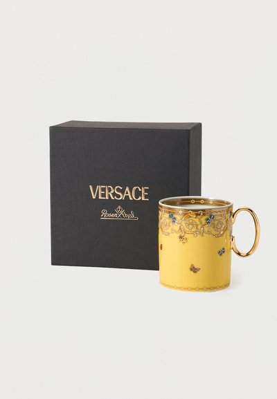 Κίτρινο πορσελάνινο φλιτζάνι με χρυσή λαβή, περίτεχνα σχέδια με λουλούδια και πεταλούδες, τοποθετημένο δίπλα σε μαύρο κουτί με την επωνυμία Versace Rosenthal.
