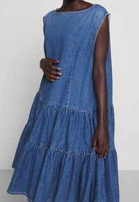 Džínové šaty s kulatým výstřihem, bez rukávů a volánkovým lemem. Mají modrou pranou barvu a uvolněný střih.