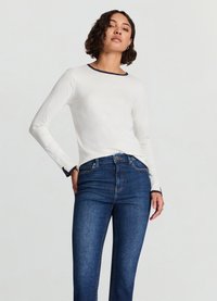 White long-sleeve top with navy collar and cuffs, paired with dark blue skinny jeans. Smooth fabric with a fitted design.