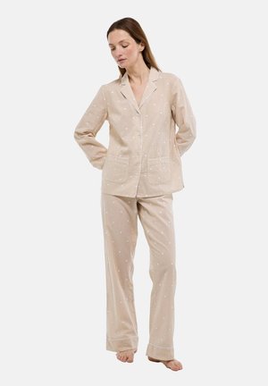 Ensemble de pyjama beige à pois blancs, comprenant une chemise boutonnée avec col cranté et un pantalon assorti à coupe droite. Matière en coton.