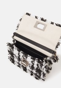 Černobílá kabelka z tvídu s roztrženými okraji, stříbrným kováním a koženým popruhem. Vnitřek je podšitý krémovým materiálem a má magnetické zapínání.