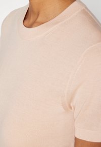 Světle růžové tričko s krátkým rukávem z měkké tkaniny, s vroubkovaným kulatým výstřihem a hladkým povrchem s minimem švů.