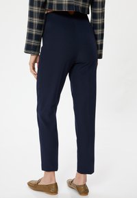 Navyblaue, hoch taillierte Hosen aus glattem Stoff, mit schmalem Schnitt und verkürzter Länge, kombiniert mit braunen Leder Slippern.